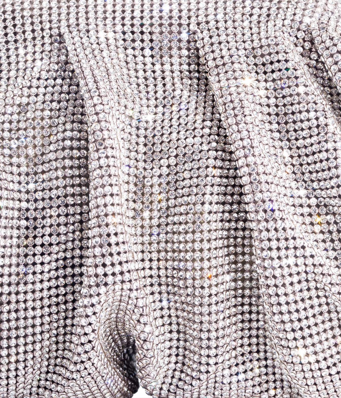 A close-up of a silver rhinestone-embellished fabric, showing the shimmering texture and draped folds of the material.