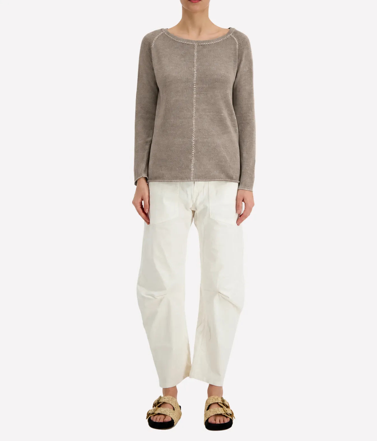 Front view of a model wearing the Avant Toi Maglia Pullover In Taupe untucked over cream barrel-leg trousers with dark sandals, showing the raglan sleeves and relaxed fit