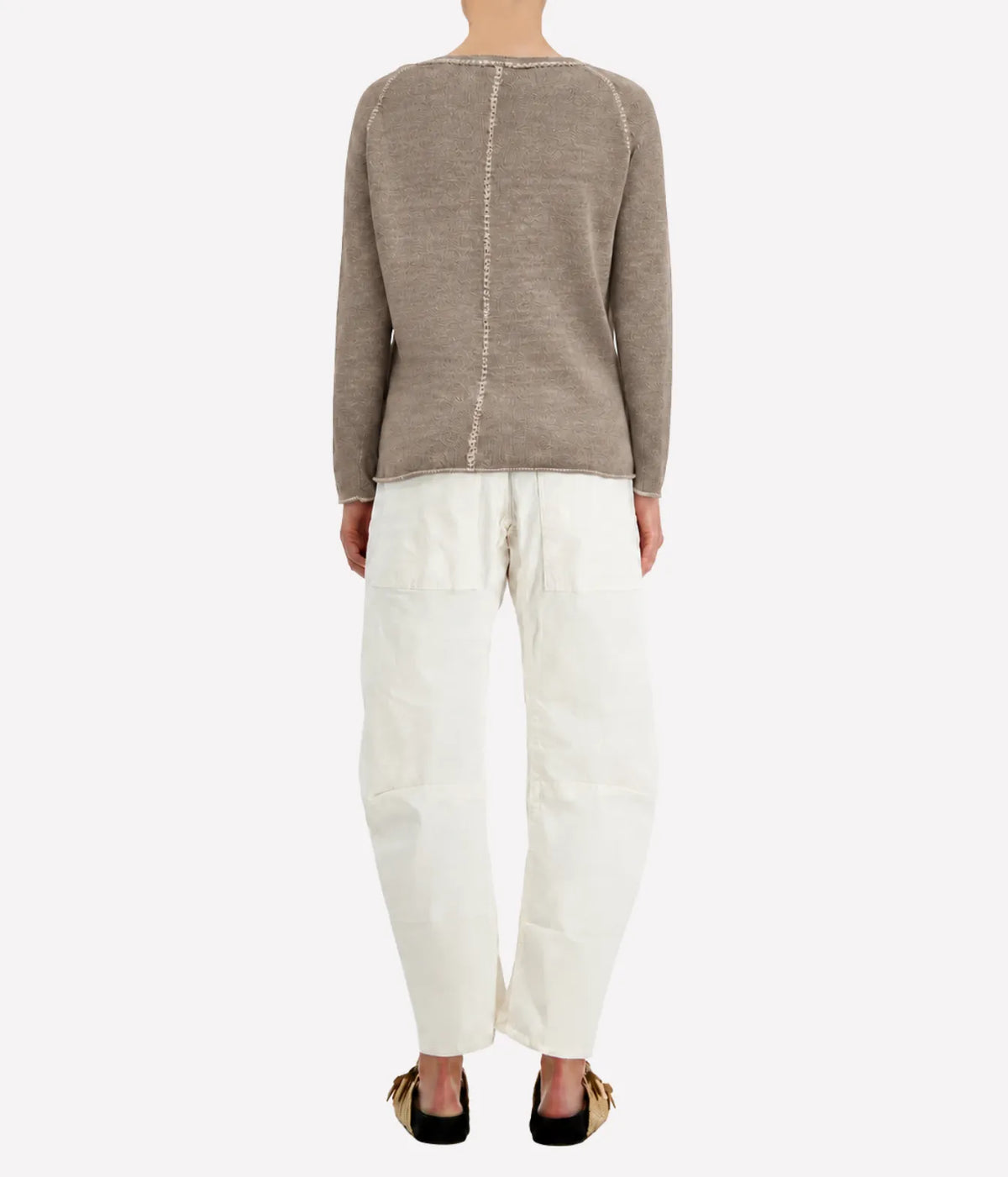 Back view of a model wearing the Avant Toi Maglia Pullover In Taupe with cream barrel-leg trousers and dark sandals, showing the contrast centre-back seam