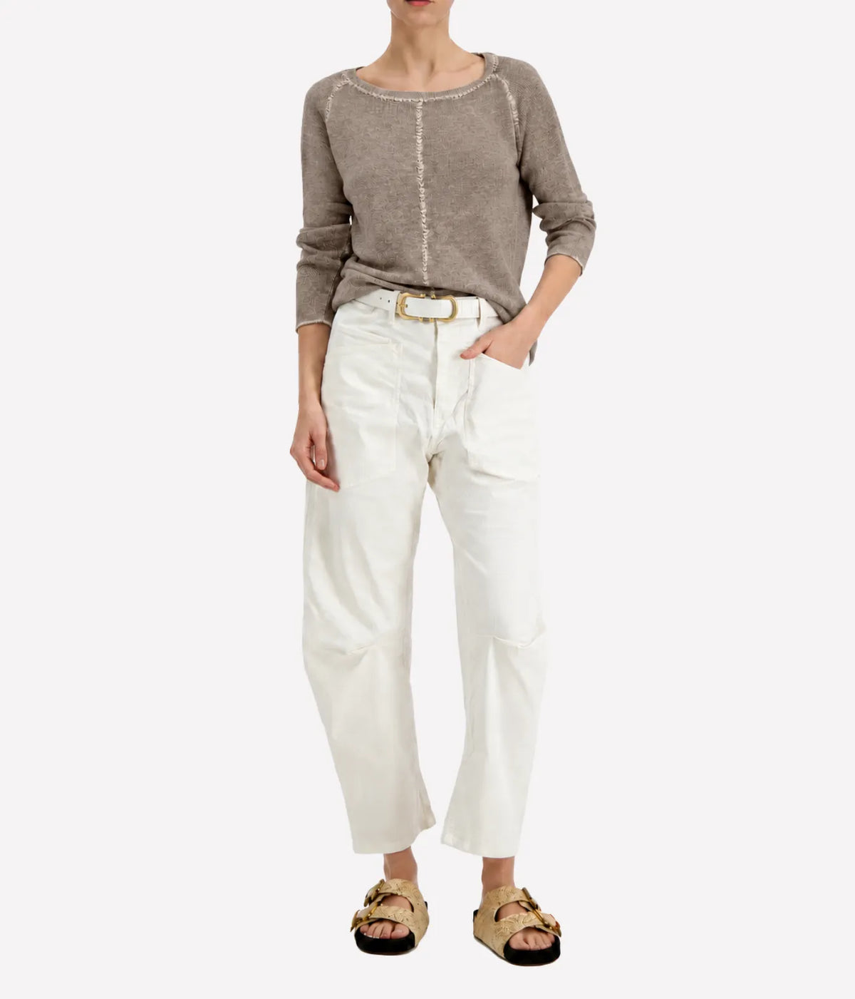 Model wearing the Avant Toi Maglia Pullover In Taupe tucked into cream barrel-leg trousers with a brown leather belt and dark sandals