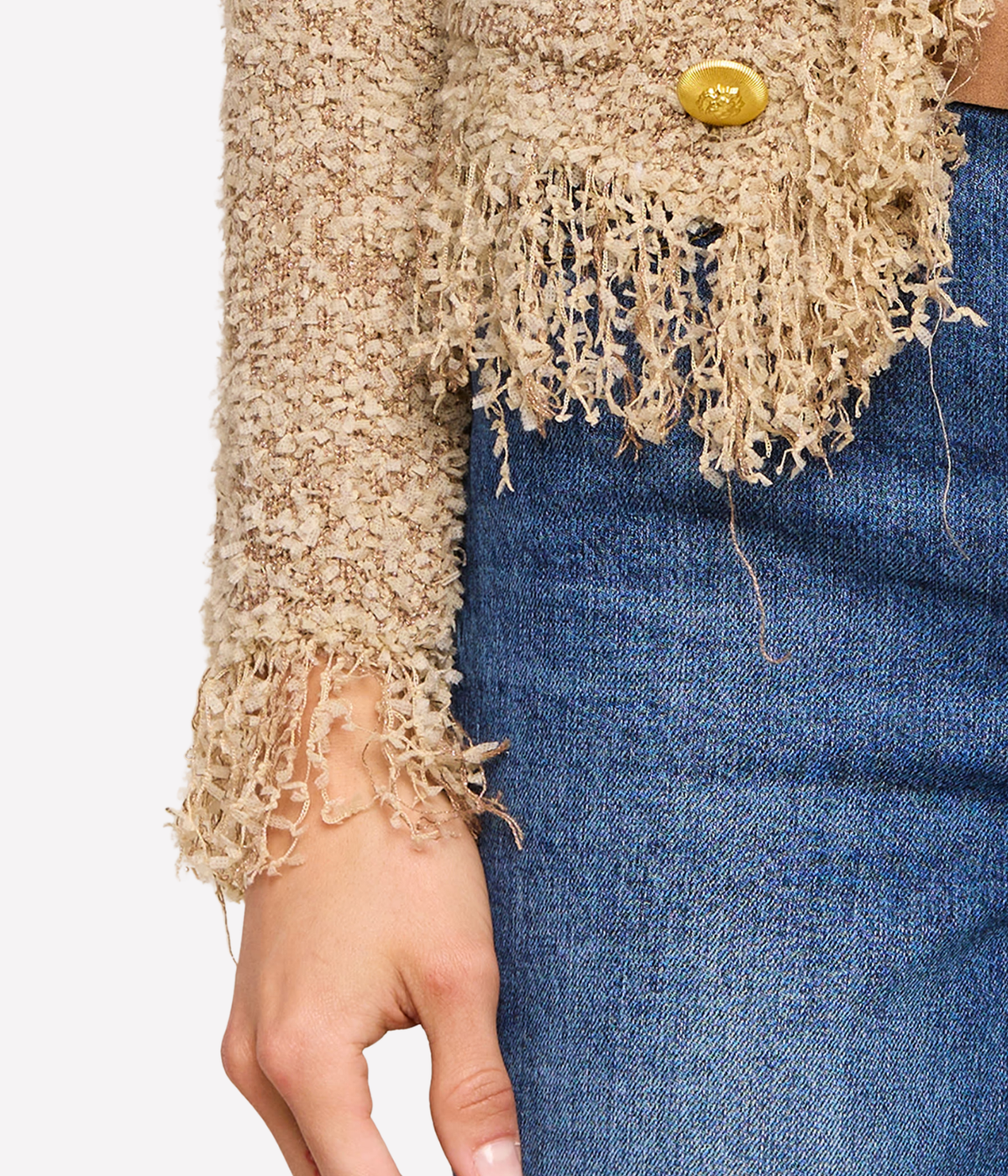Close-up of a person wearing the Mireille Fringe Cardigan in Beige with a gold button, paired with blue jeans