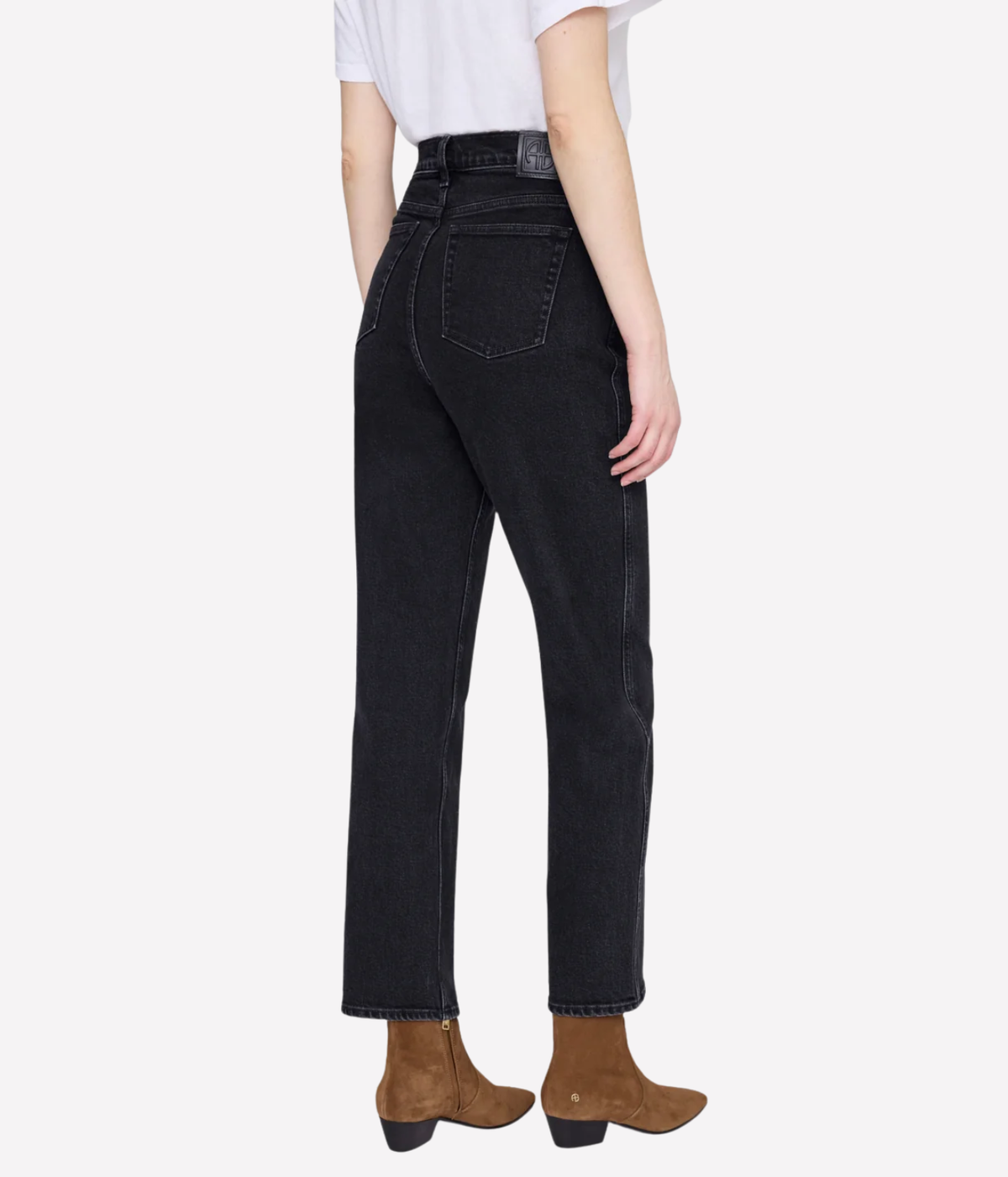 A model shown from the back wearing high-waisted black denim jeans, a white t-shirt, and brown ankle boots against a light gray background.