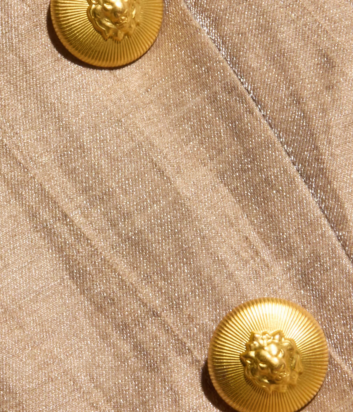 Close-up of the linen blazer with two prominent round gold buttons featuring lion head motifs.