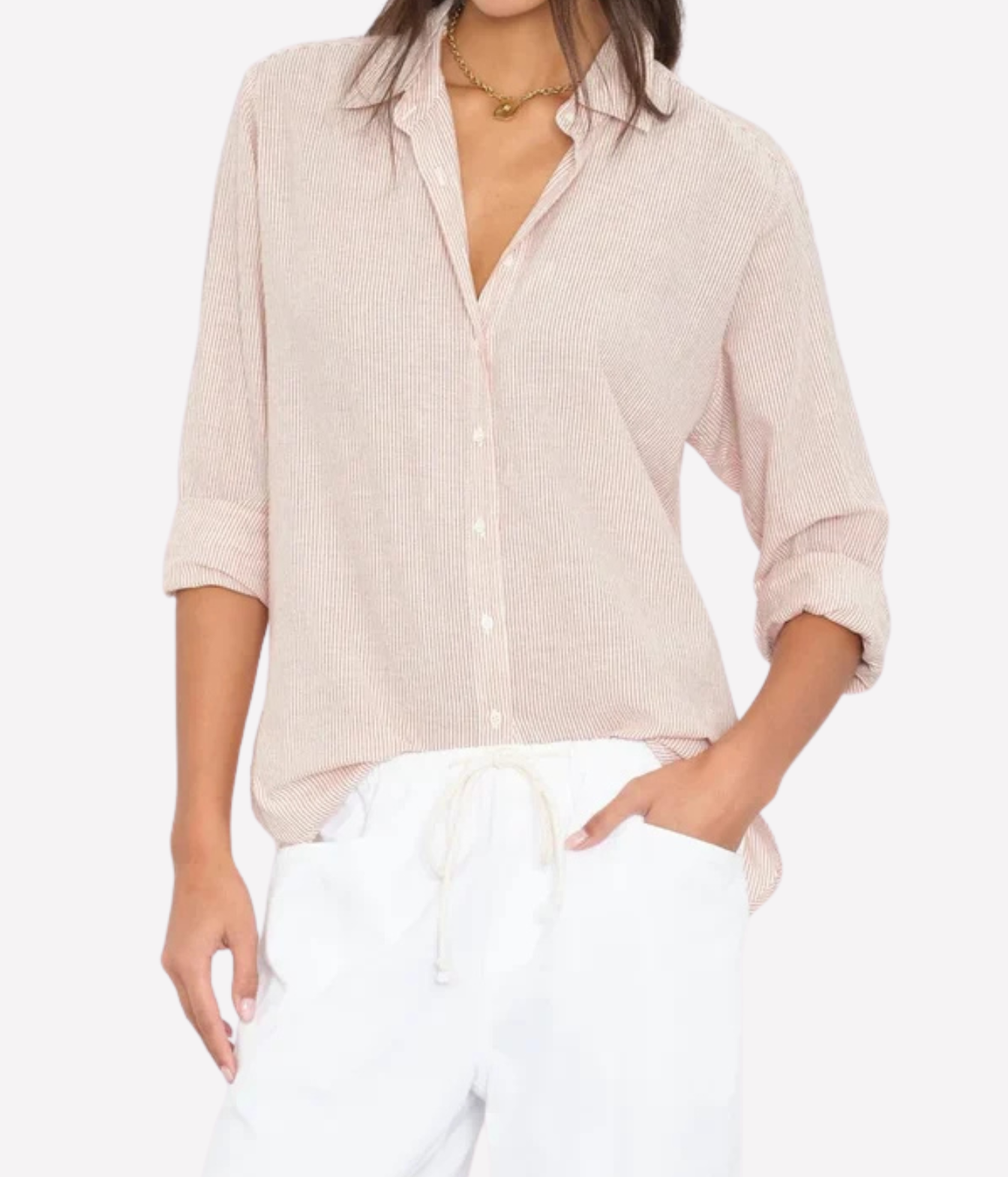 A woman wearing a light pink textured button-up shirt with rolled sleeves and white drawstring pants, photographed against a plain light background.
