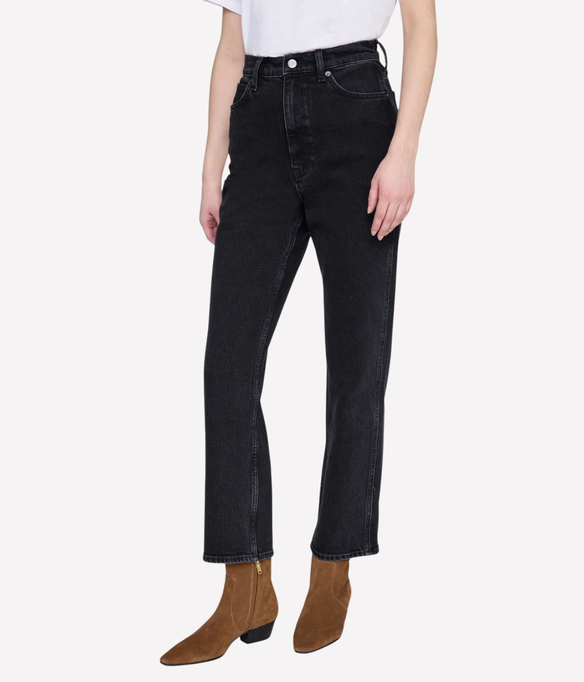 A model wearing a pair of black high-rise straight-leg jeans with brown suede ankle boots, shown from the waist down on a light gray background.