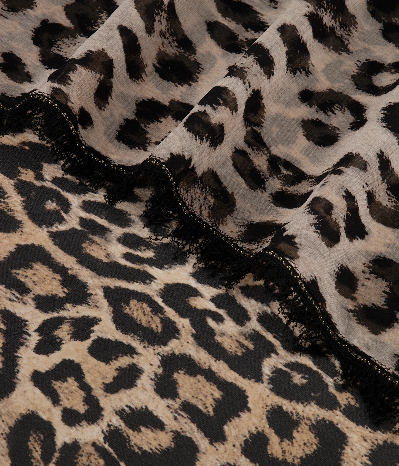 Leopard print fabric with black and beige animal spots, draped to show texture and a black fringed edge.