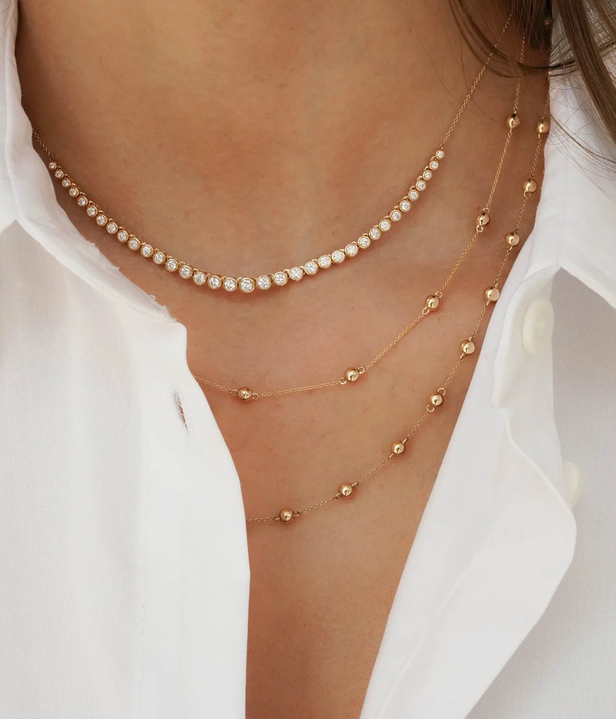 Model wearing the Dana Rebecca Designs Lulu Jack Graduating Bezel Tennis Necklace in 14k Yellow Gold layered with fine gold beaded chains under an open white shirt