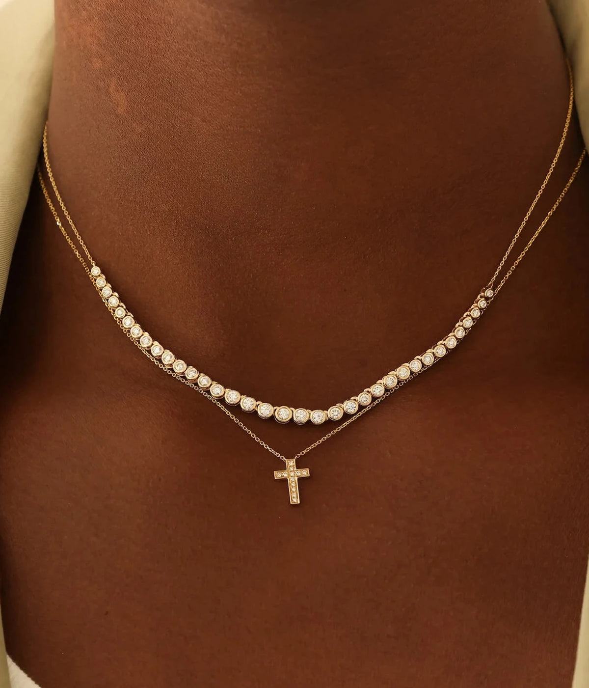 Model wearing the Dana Rebecca Designs Lulu Jack Graduating Bezel Tennis Necklace in 14k Yellow Gold layered above a fine gold chain with a small cross pendant