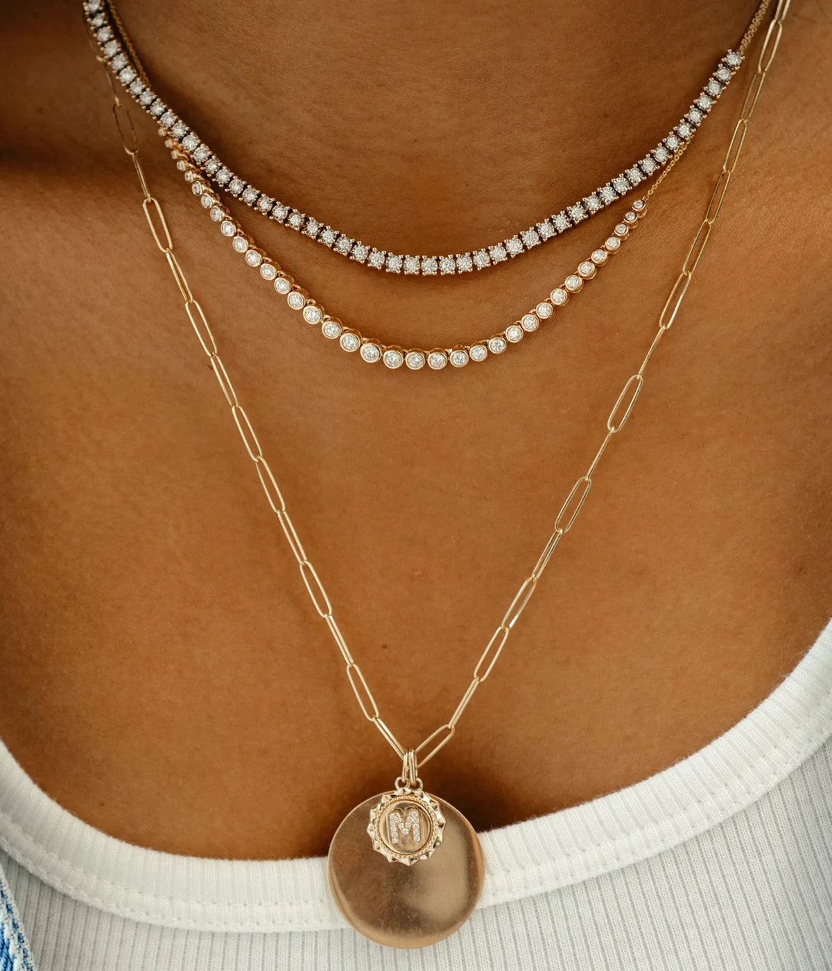 Model wearing the Dana Rebecca Designs Lulu Jack Graduating Bezel Tennis Necklace in 14k Yellow Gold stacked with a second tennis necklace and a long gold medallion chain, with a white tank