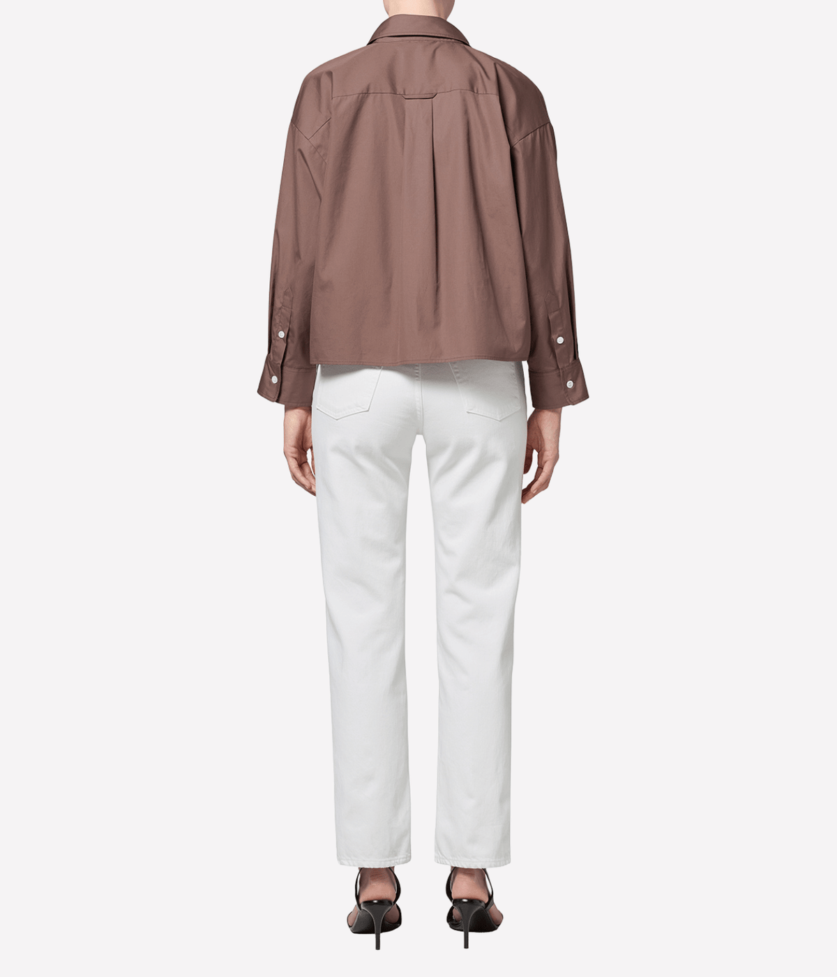 Back view of a model wearing the Citizens Of Humanity 90s French High Rise Straight in vintage white with a brown shirt and black strappy heels, showing the back of the straight leg and hem