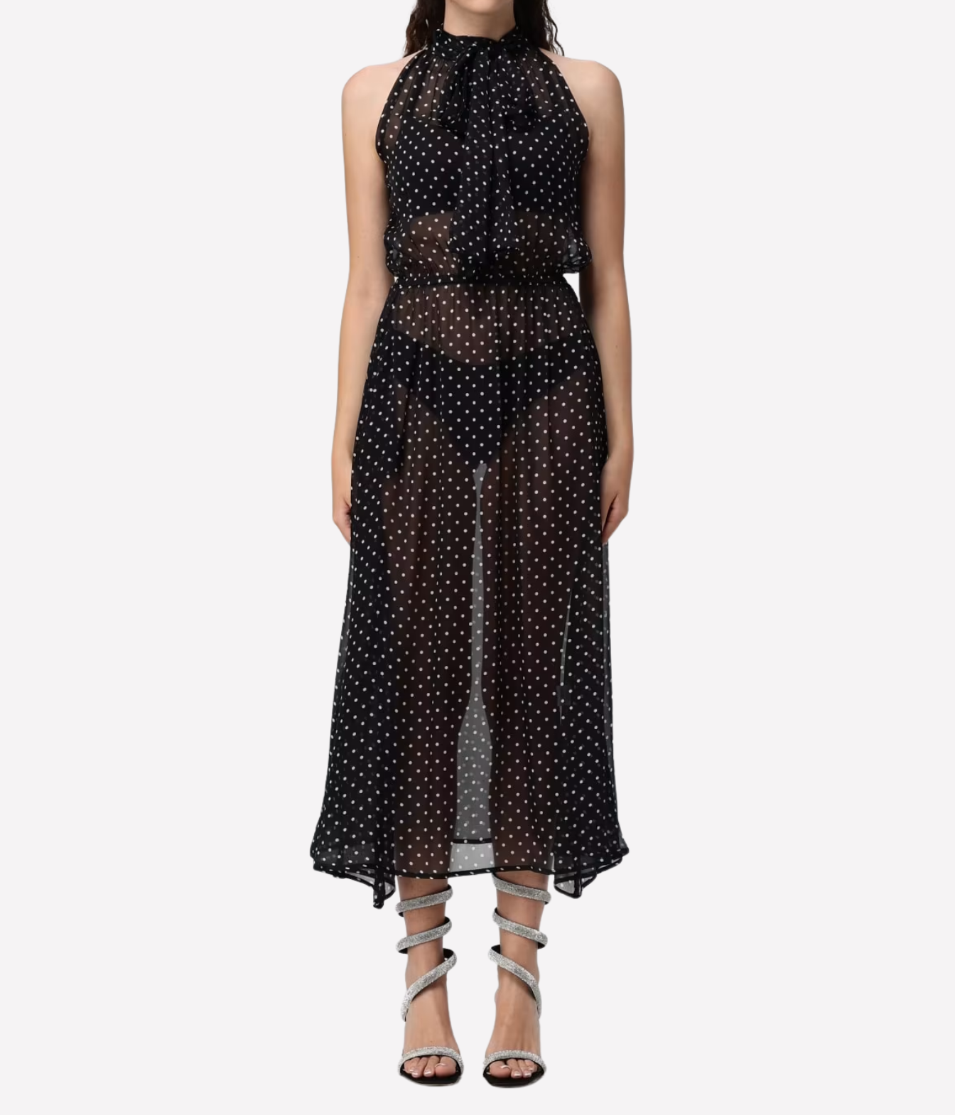 A sleeveless black sheer mesh maxi dress with a white polka dot pattern, featuring a high halter neckline and a tie at the collar, modeled against a light gray background.
