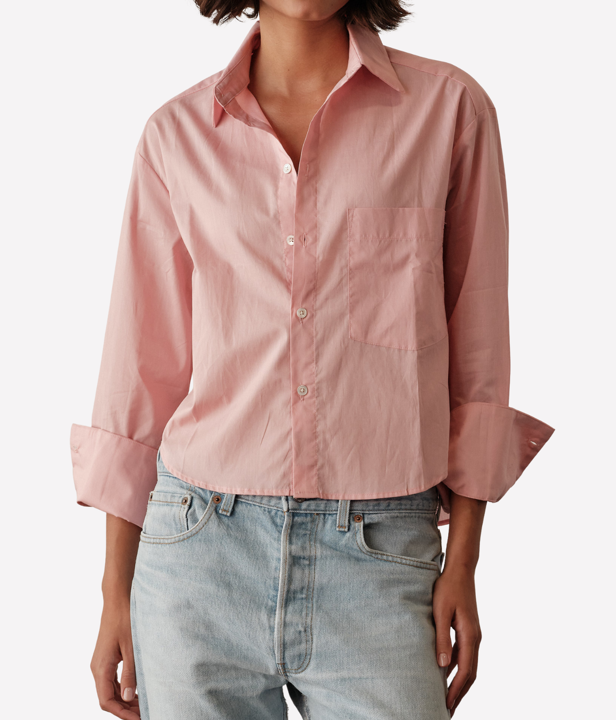 Close-up front view of a model wearing the CISSA Belle Shirt in Blossom partly unbuttoned at the collar with wide turned-back cuffs, showing the chest pocket and curved cropped hem over light-wash jeans