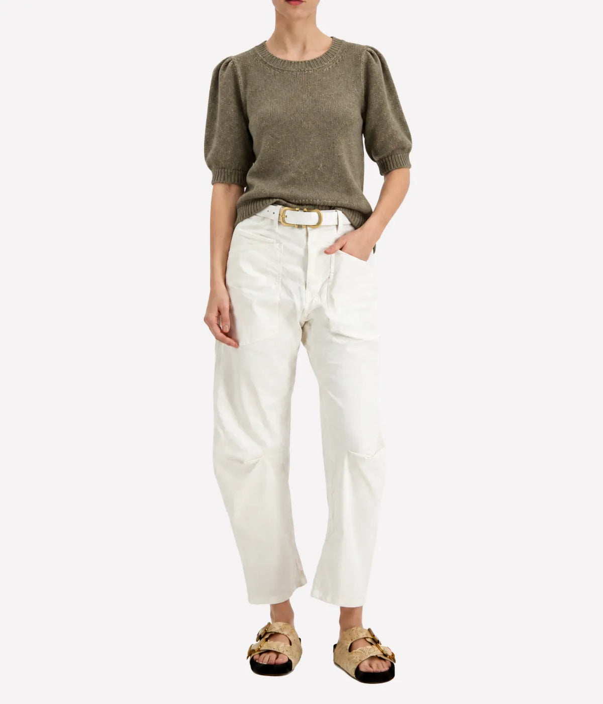 Model wearing the Avant Toi Cashmere Short Sleeve in Mushroom tucked into cream barrel-leg trousers with one hand in her pocket and dark sandals