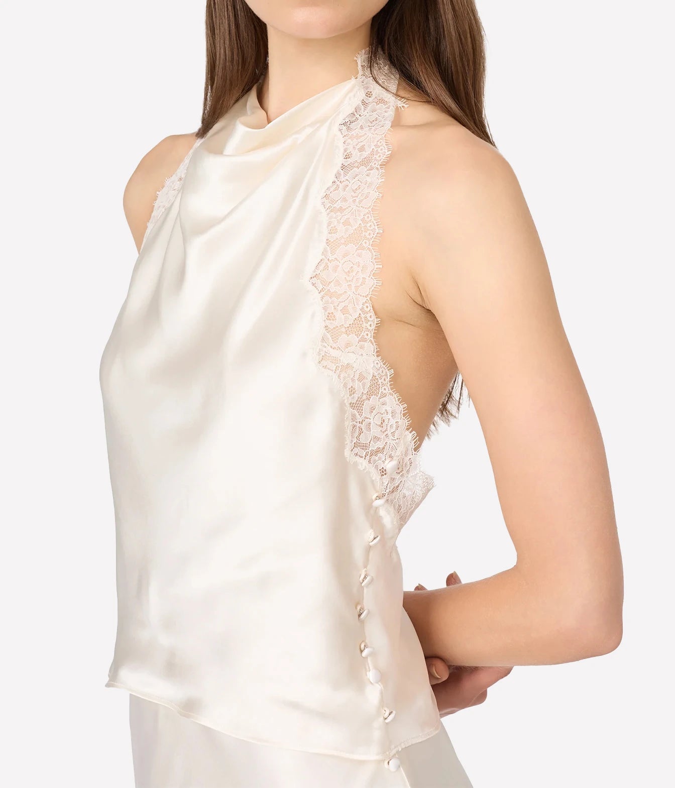 A close-up of a model wearing a cream satin halter top with intricate lace