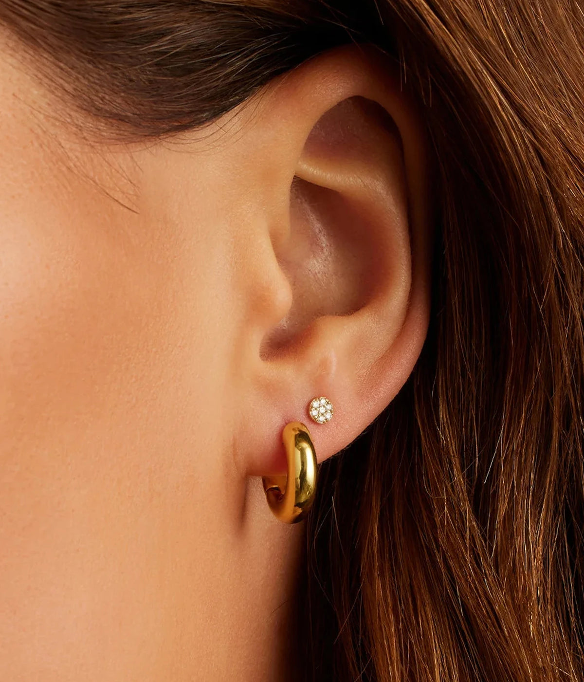Close-up of a model's ear wearing the Gorjana Lou Huggies in Yellow Gold in the lobe, with her dark hair tucked behind her ear