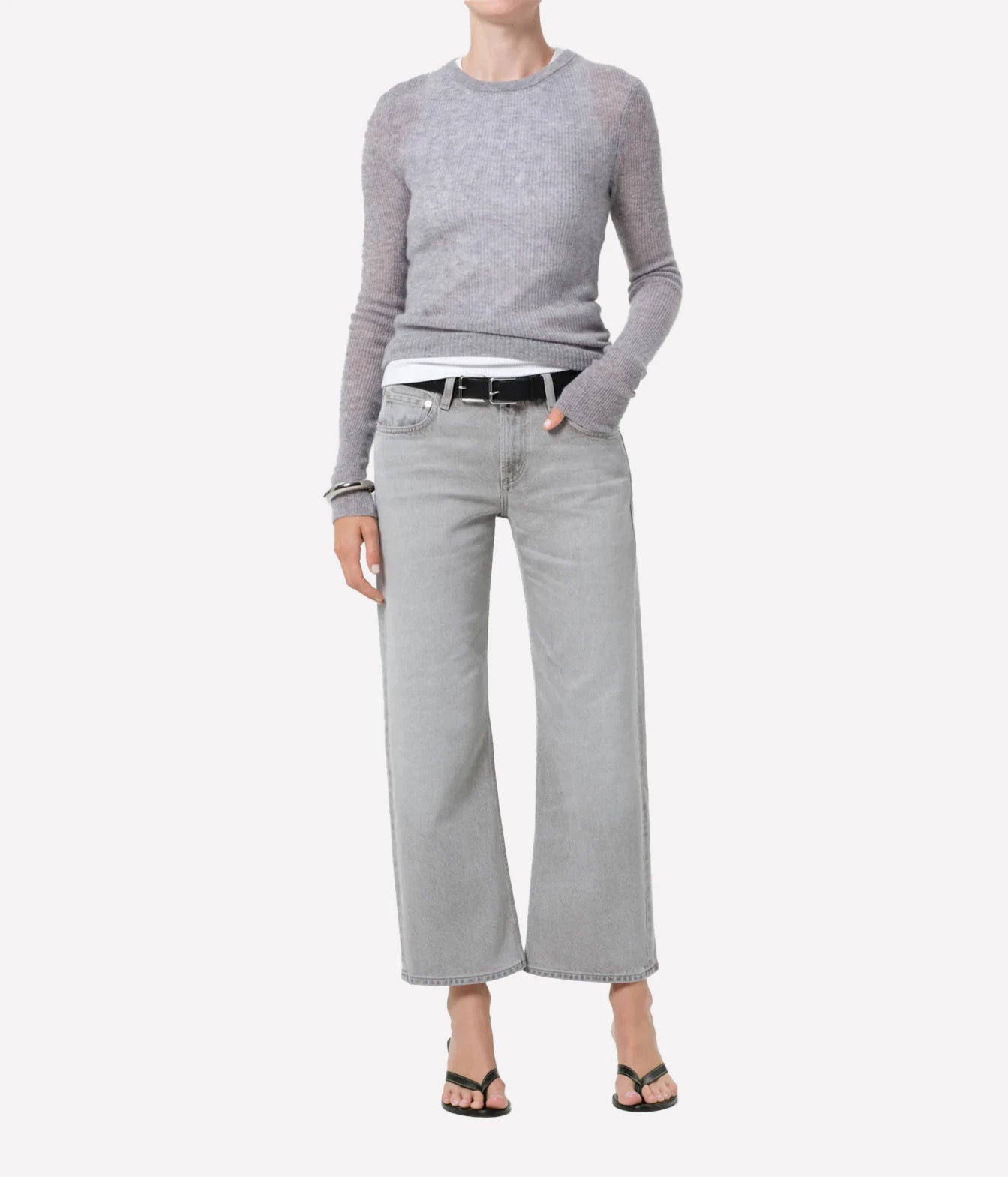 A model wearing a light gray long-sleeve knit sweater, wide-leg light gray jeans, a black belt, and black sandals, shown against a plain light gray background.