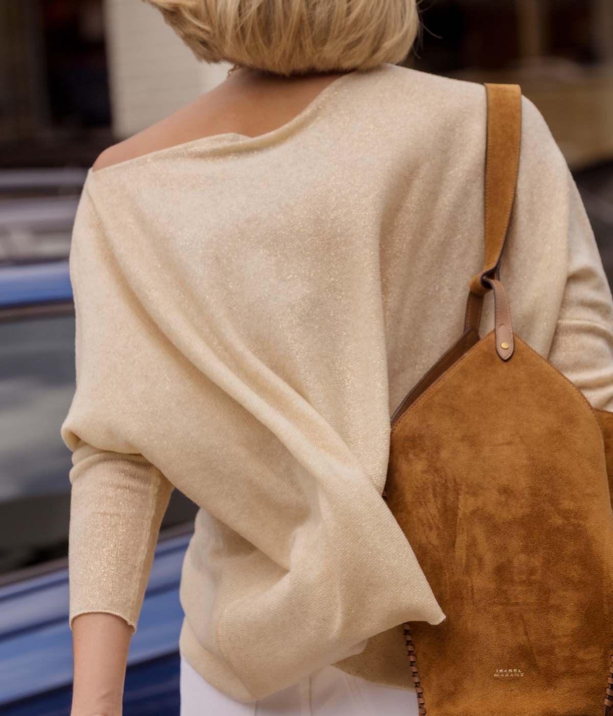 Person wearing a beige sweater and carrying a brown leather bag.