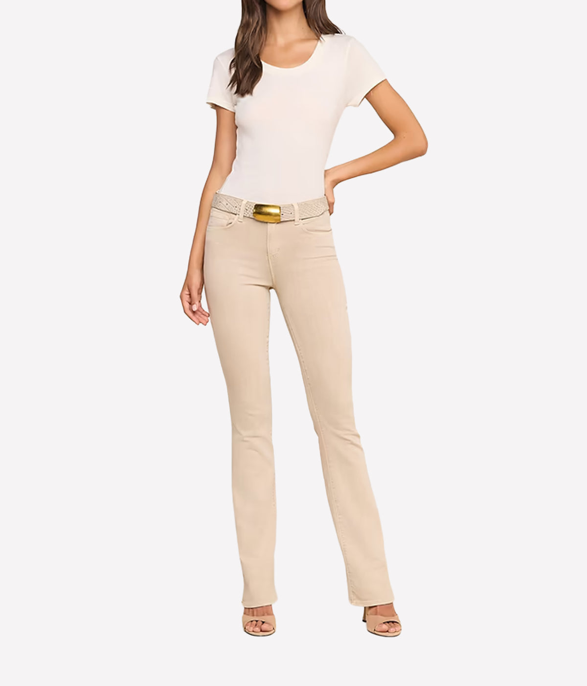 A model wearing the L'AGENCE Selma Bootcut Jean in Biscuit with a textured woven belt and a gold buckle, paired with a cream t-shirt and beige heels.
