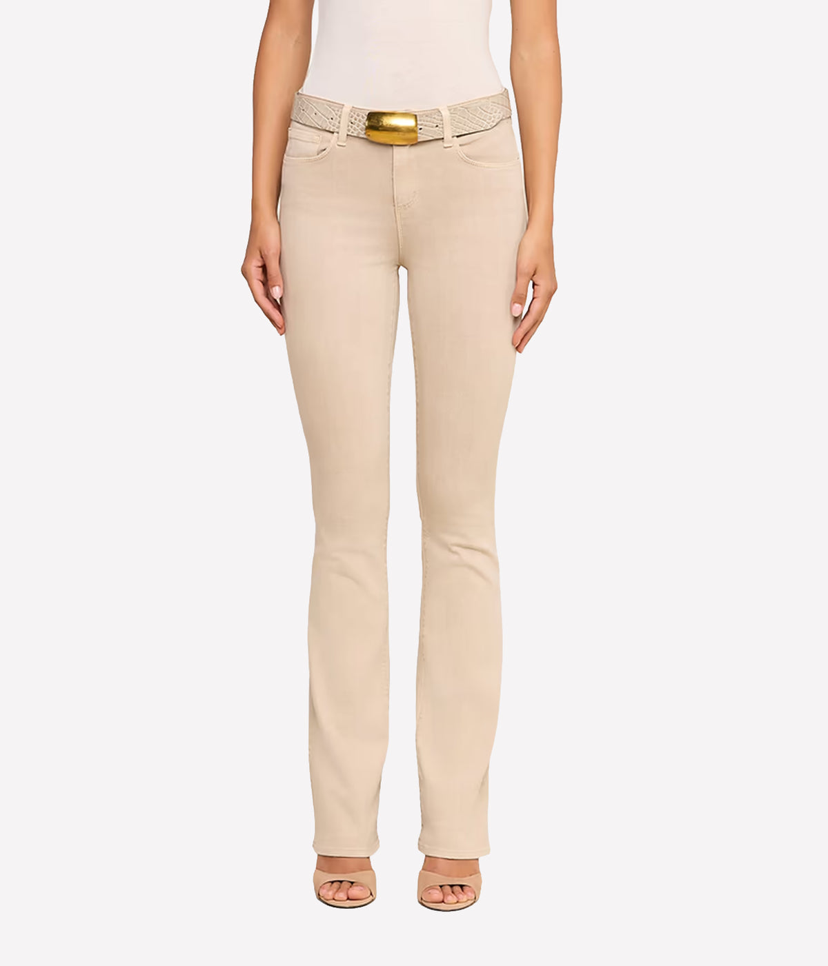A model wearing a pair of the L'AGENCE Selma Bootcut Jean in Biscuit with a matching textured belt, paired back with a white top and beige heeled sandals, shown from the waist down.