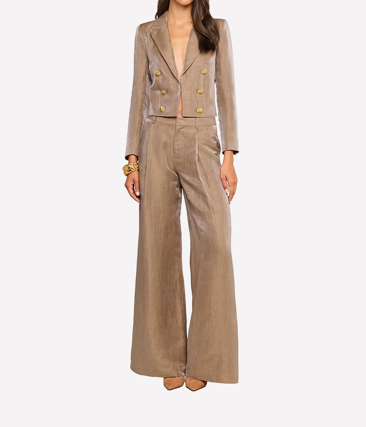A model wears a beige double-breasted blazer with gold buttons and matching wide-leg trousers, styled with gold bracelets and nude heels against a light gray background.