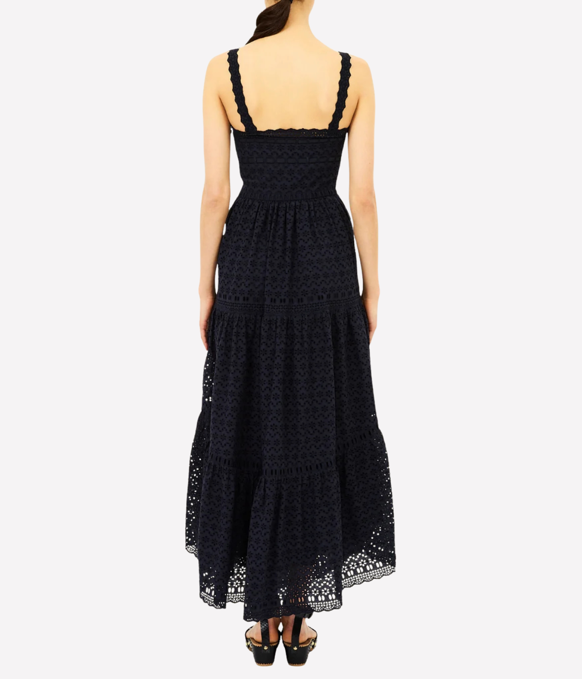 A woman modeling a sleeveless black lace maxi dress from the back, featuring a structured bodice, wide shoulder straps, and a tiered skirt, set against a plain light gray background.