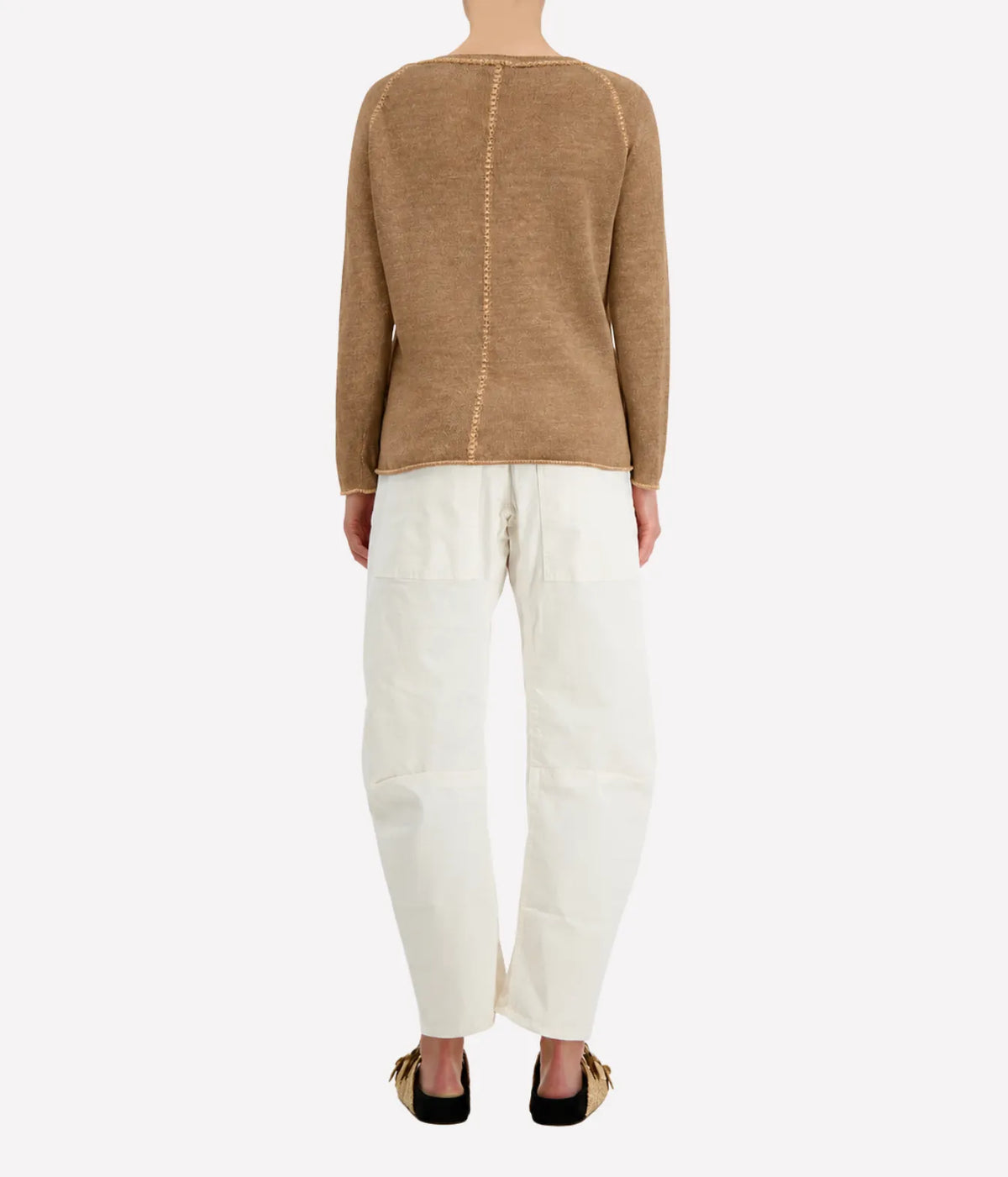 Back view of a model wearing the Avant Toi Maglia Pullover in Sughero with cream barrel-leg trousers and dark sandals, showing the contrast centre-back seam