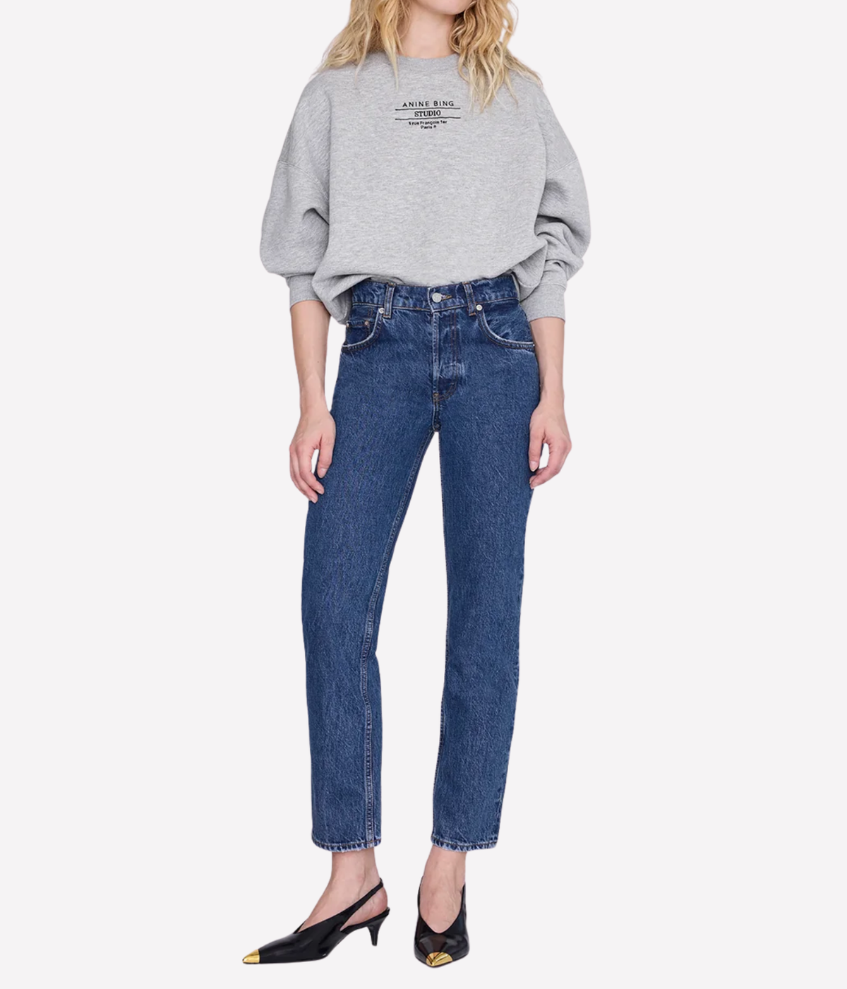 Model wearing the Anine Bing Nelly Slingback Metal Toe in Black with mid-blue straight-leg jeans with frayed cropped hems and a grey marl sweatshirt with a black graphic print