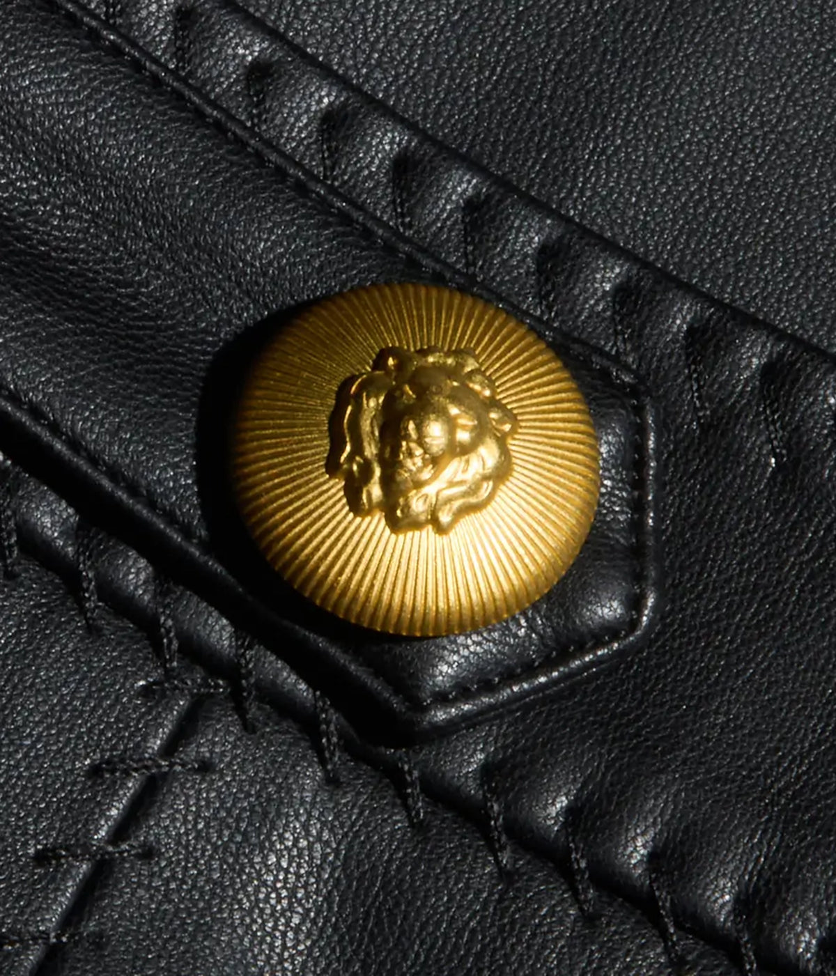 Close-up of a black vegan leather mini skirt featuring a round gold-tone button