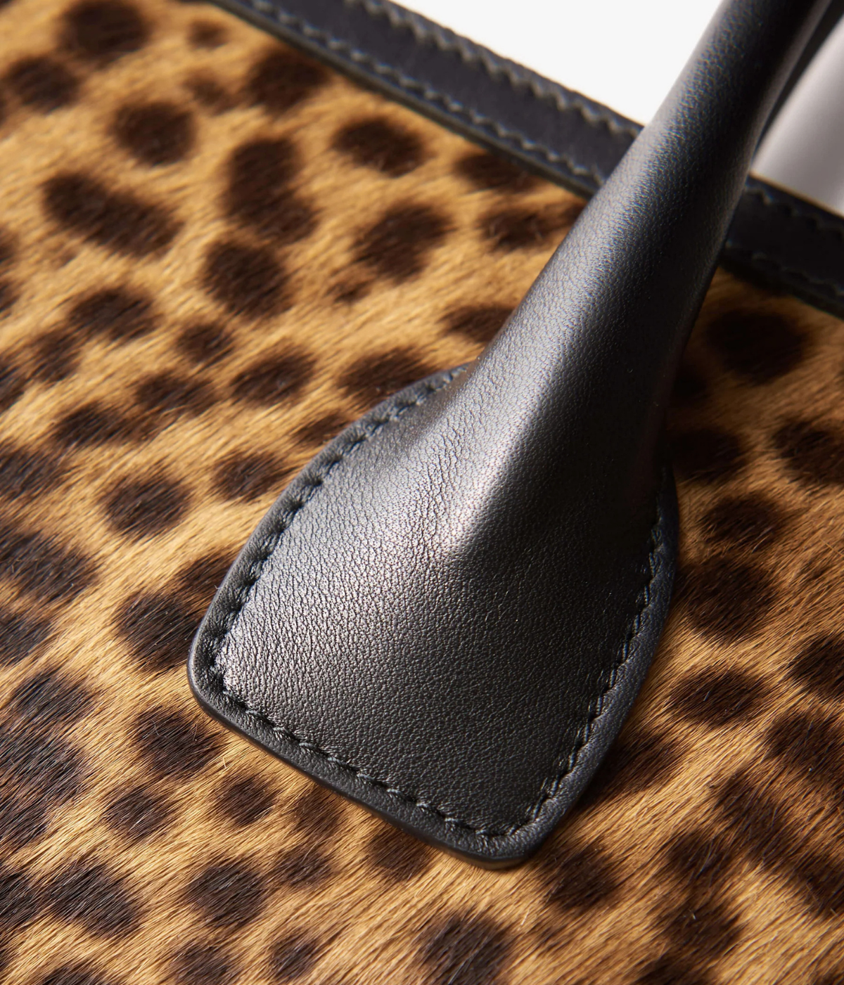Close-up of a leopard-print handbag with dark charcoal gray leather trim and a matching handle attachment.