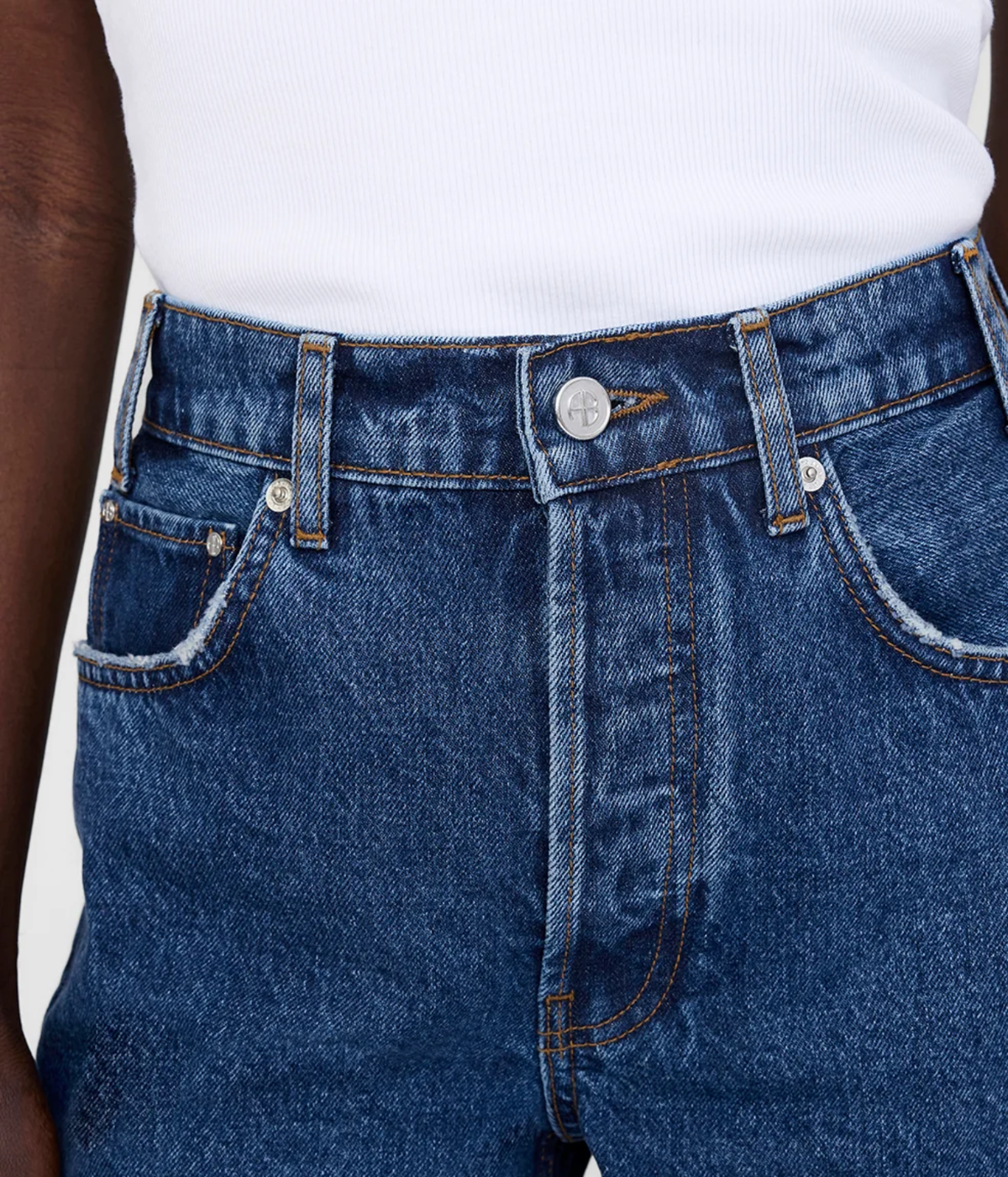 Close-up of a person wearing dark blue denim jeans with a white ribbed top visible at the waist.