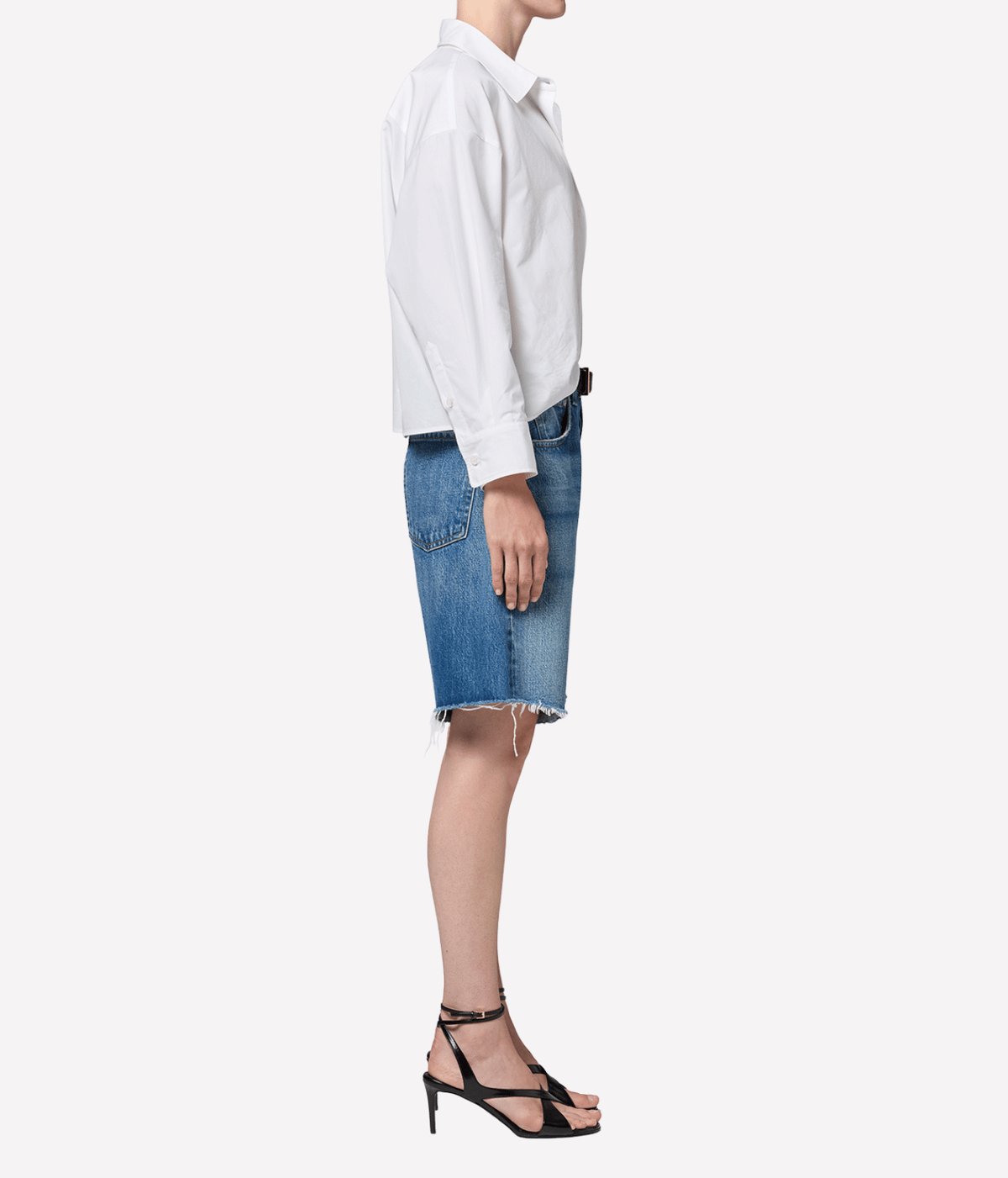 Side profile of a model wearing the Citizens of Humanity Ayla Short in Chaya with a white shirt and black strappy heeled sandals, showing the relaxed longline fit that sits at the knee