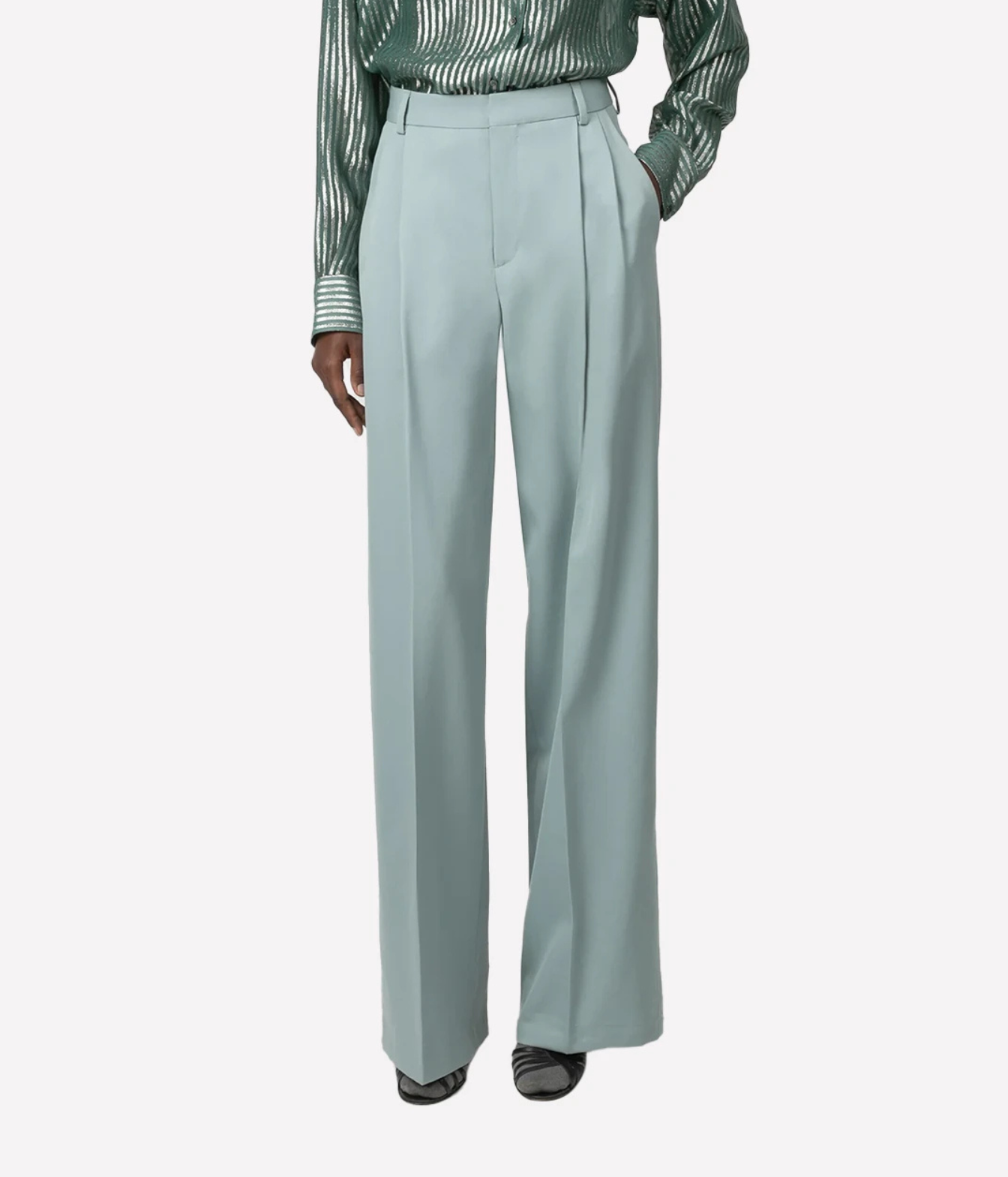 A model is shown wearing wide-leg sage green trousers, paired with black pointed shoes, against a light gray background.