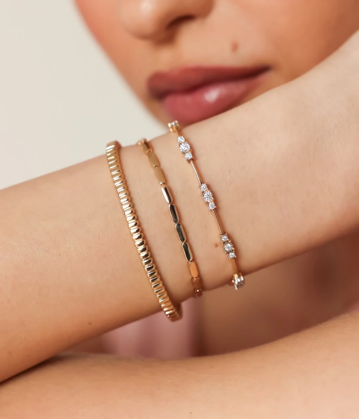 Close-up of a model's wrist raised to her chin wearing the Dana Rebecca Designs Ava Bea Spaced Tennis Bracelet in 14k Yellow Gold stacked with two fine gold chain bracelets