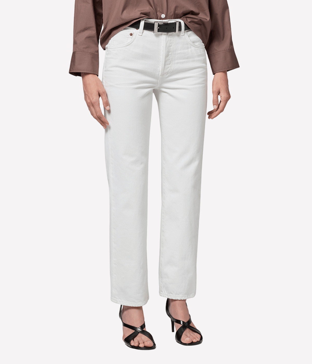 Close-up of a model wearing the Citizens Of Humanity 90s French High Rise Straight in vintage white with a brown button-up shirt, black leather belt with a silver buckle and black strappy heeled sandals, showing the straight leg and front pockets