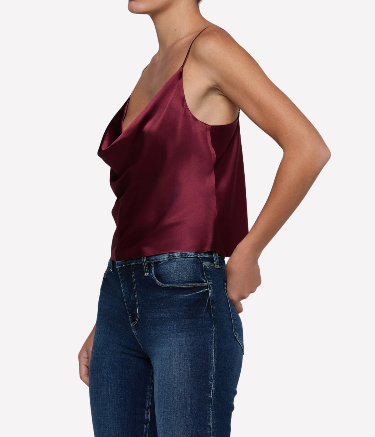 A woman wearing a deep burgundy silk camisole top with thin straps and blue jeans, shown from a side profile.