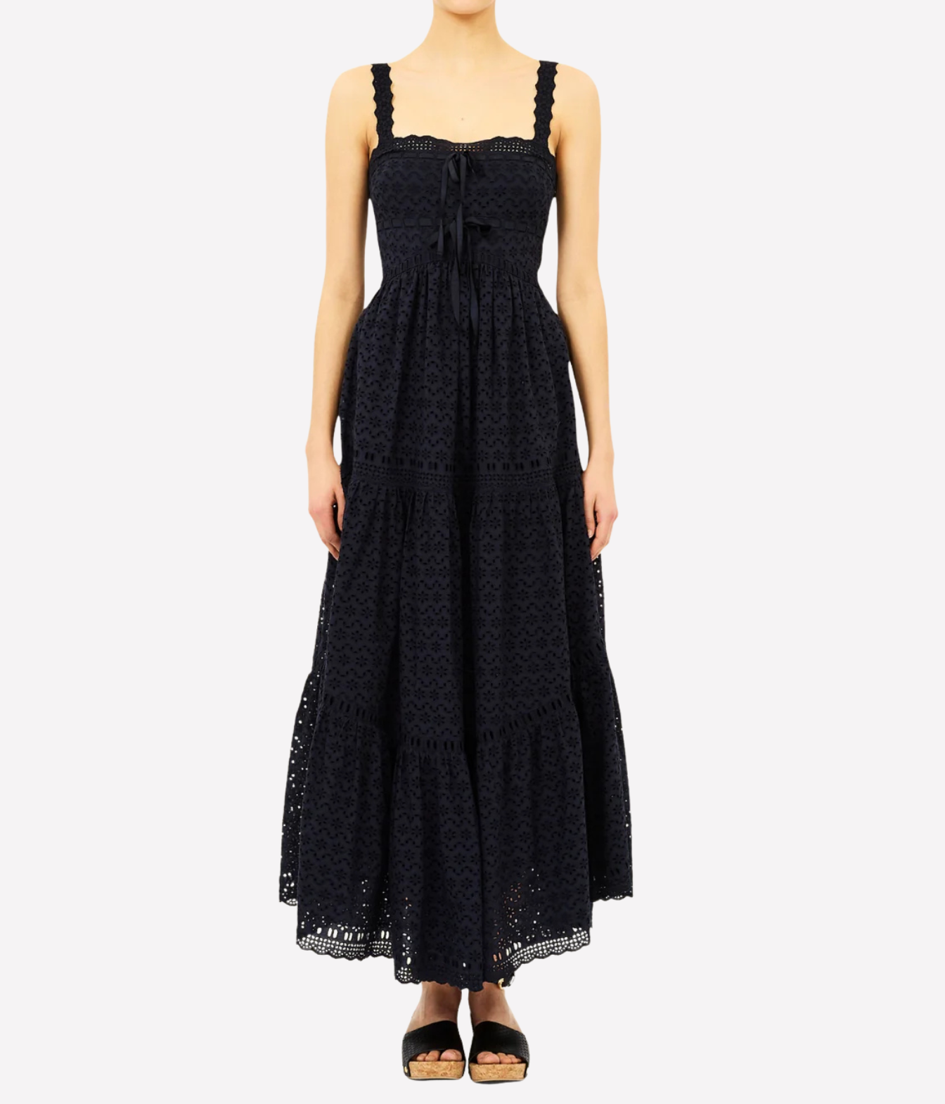 A woman modeling a black lace maxi dress with a tie-front bodice and tiered skirt, paired with black sandals, against a light gray studio background.