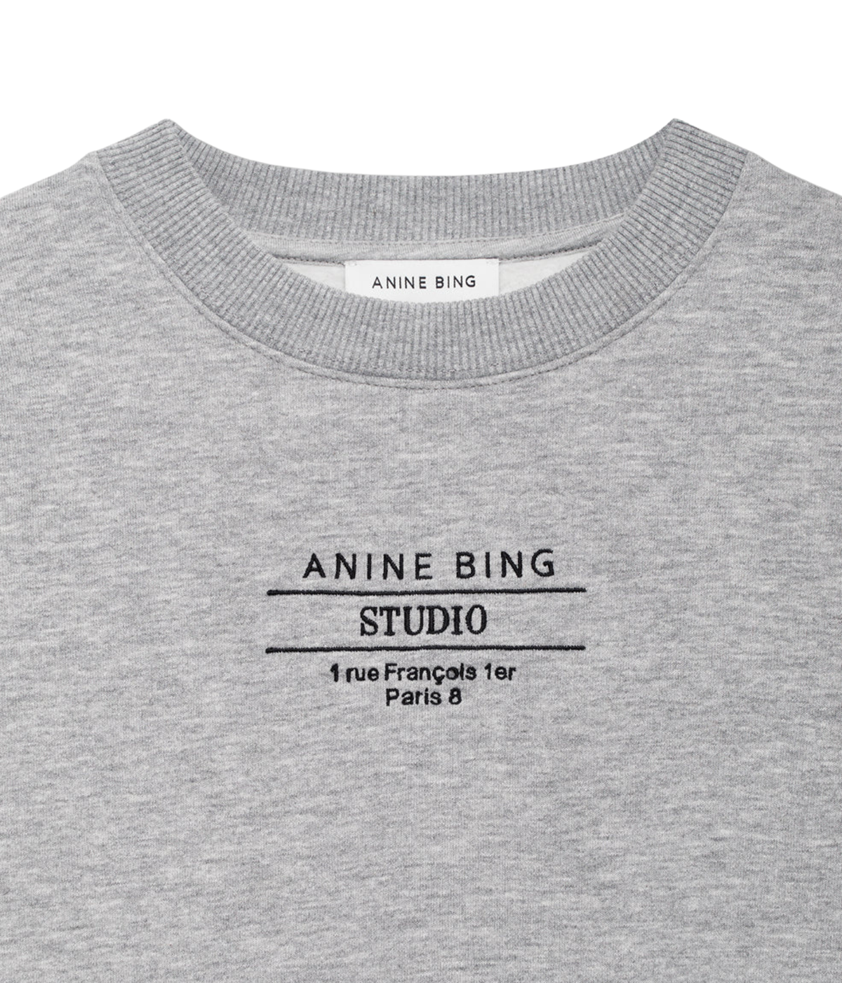 Close-up of a heather gray crewneck sweatshirt with black printed text reading 'ANINE BING STUDIO' and a small address below, on a white background.