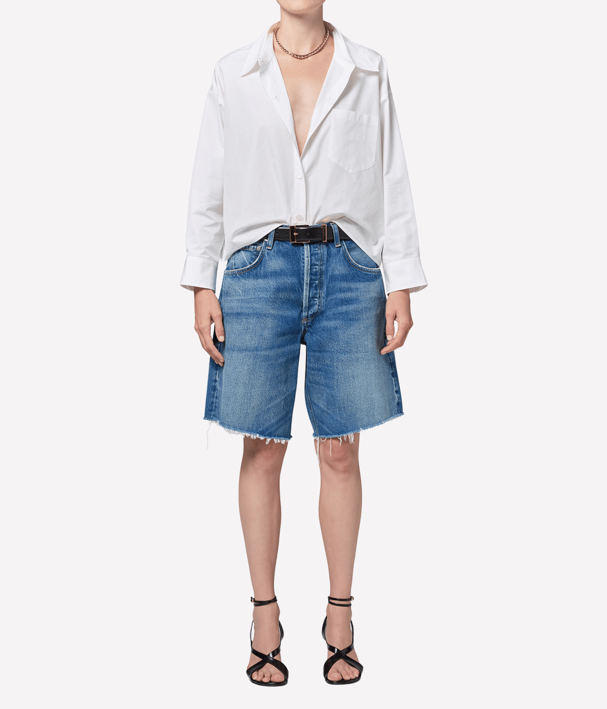 Model wearing the Citizens of Humanity Ayla Short in Chaya with a white shirt open at the collar and sleeves pushed up, a black leather belt, a gold necklace and black strappy heeled sandals