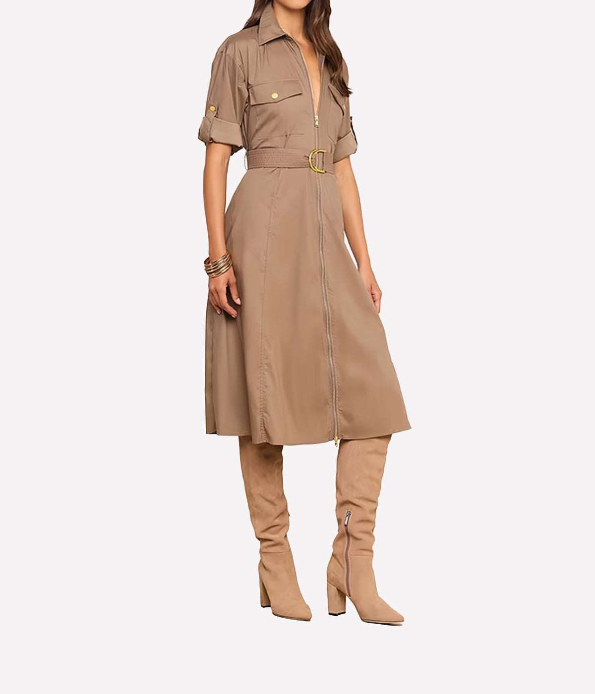 A woman models a tan utility shirt dress with short sleeves, a collar, a front zipper, a matching belt with a gold buckle, and matching tan over-the-knee boots against a light grey background.