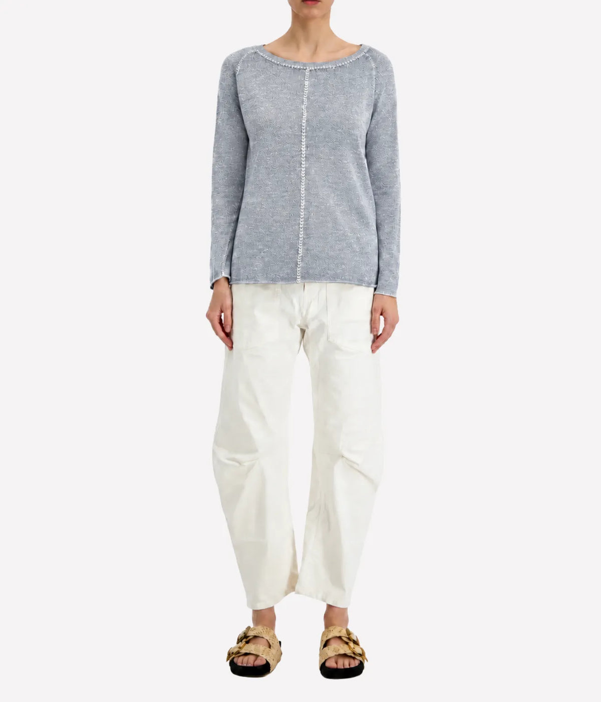 Front view of a model wearing the Avant Toi Maglia Pullover In Dusty Blue untucked over cream barrel-leg trousers with dark sandals, showing the raglan sleeves and relaxed fit