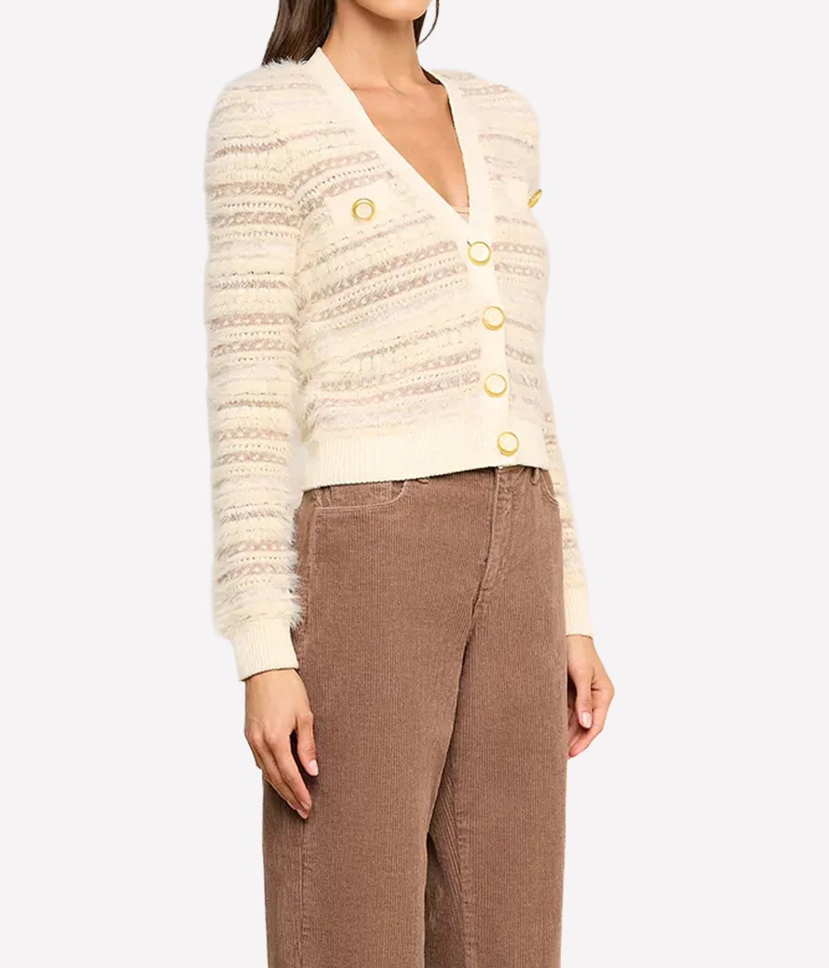 A model wearing a cream-coloured textured knit cardigan with gold buttons and brown corduroy trousers, angled view.