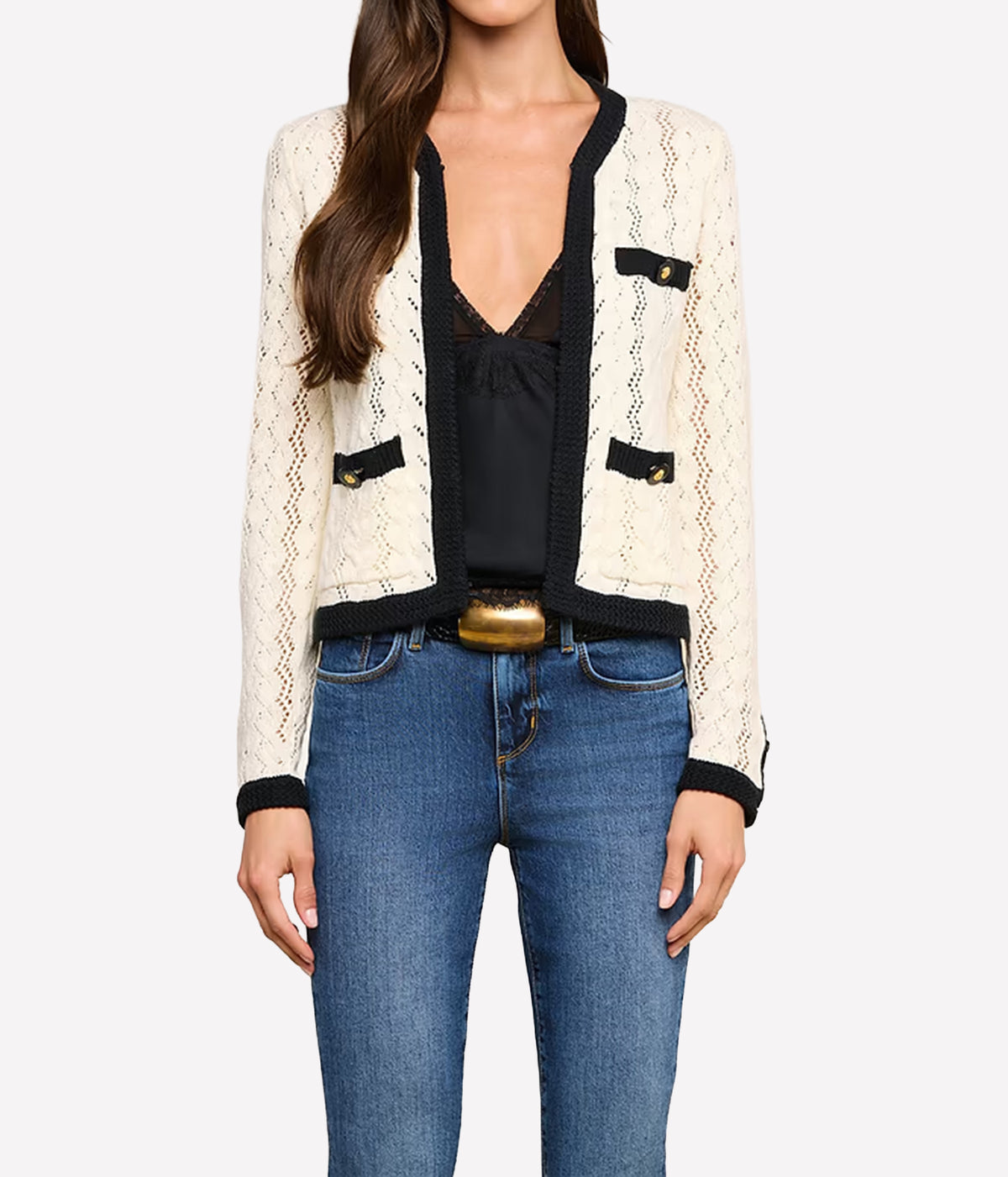 A woman wearing the L'AGENCE Zephyra Pointelle Knit Cardigan in Ivory & Black with black trim and gold-tone button details, styled over a black top and blue jeans.