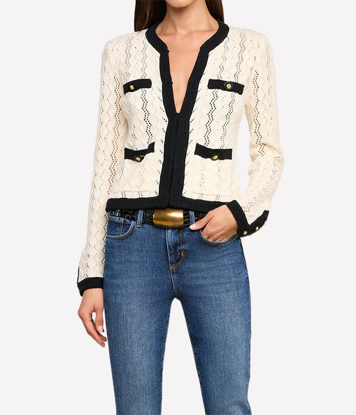 A woman wearing the L'AGENCE Zephyra Pointelle Knit Cardigan in Ivory & Black with black trim and gold buttons, paired with blue jeans and a gold belt.