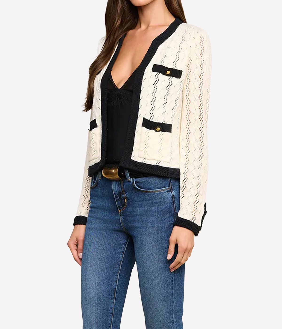 A woman wearing the L'AGENCE Zephyra Pointelle Knit Cardigan in Ivory & Black with gold-tone button accents, styled over a black top and blue jeans.