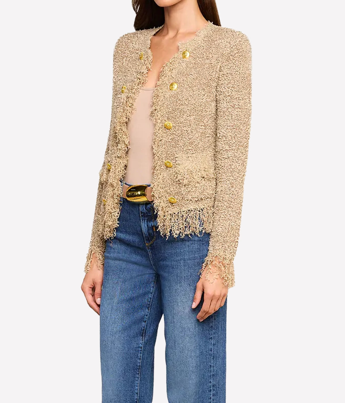 Woman wearing the Mireille Fringe Cardigan, a textured beige confetti knit cardigan with subtle metallic threads and gold buttons, layered over a nude top and blue jeans.