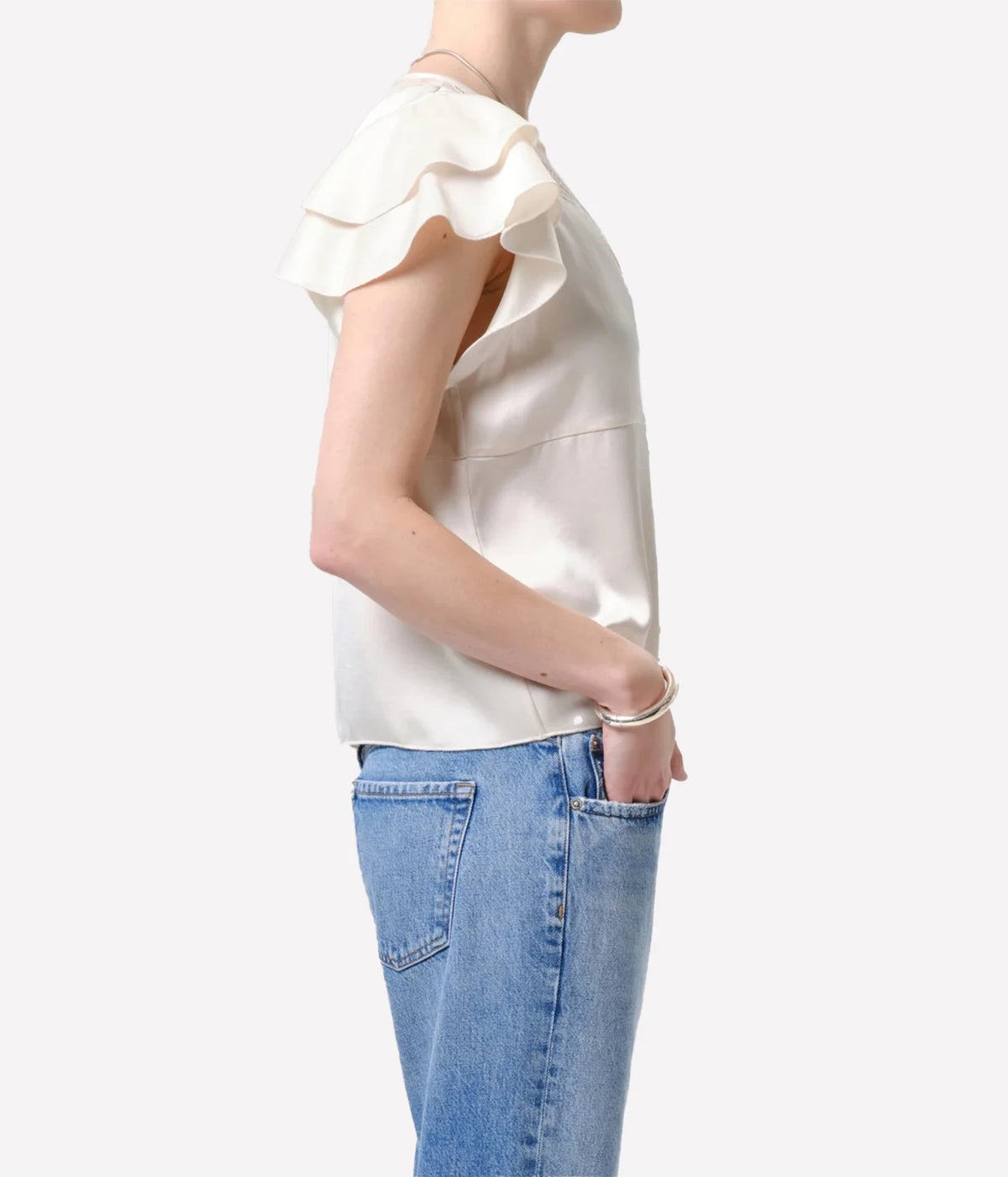 Side profile of a model wearing the Citizens Of Humanity Lola Flutter Lace Sleeve Top in Cream with mid-wash jeans and a hand in her pocket, showing the layered flutter sleeves and relaxed fit