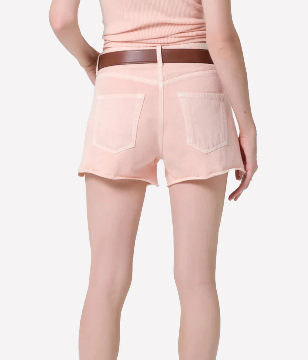 A model shown from the back wearing light pink denim shorts with a brown belt - Citizens of Humanity Marlow Denim Short in Pale Coral
