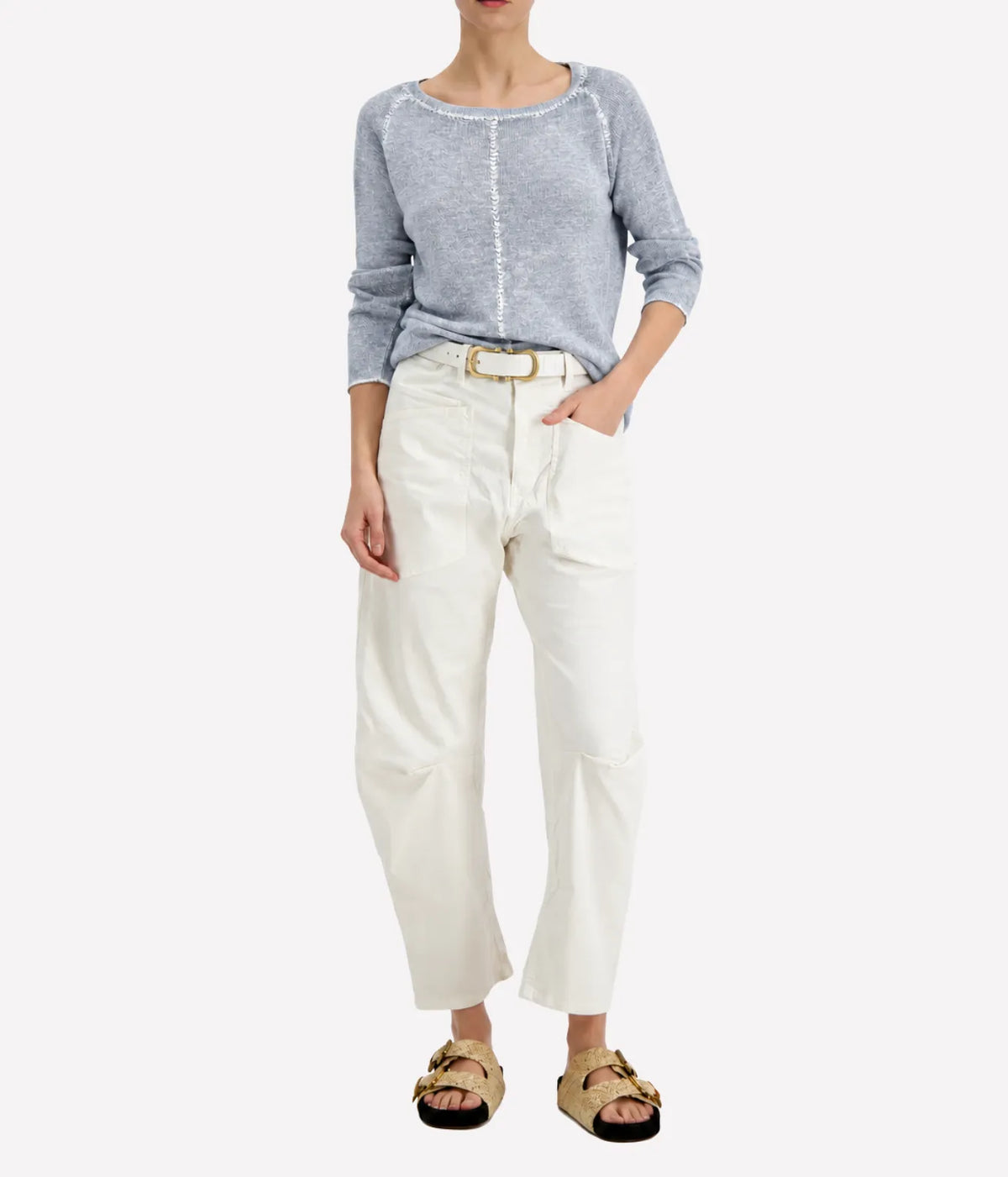 Model wearing the Avant Toi Maglia Pullover In Dusty Blue tucked into cream barrel-leg trousers with a brown leather belt and dark sandals