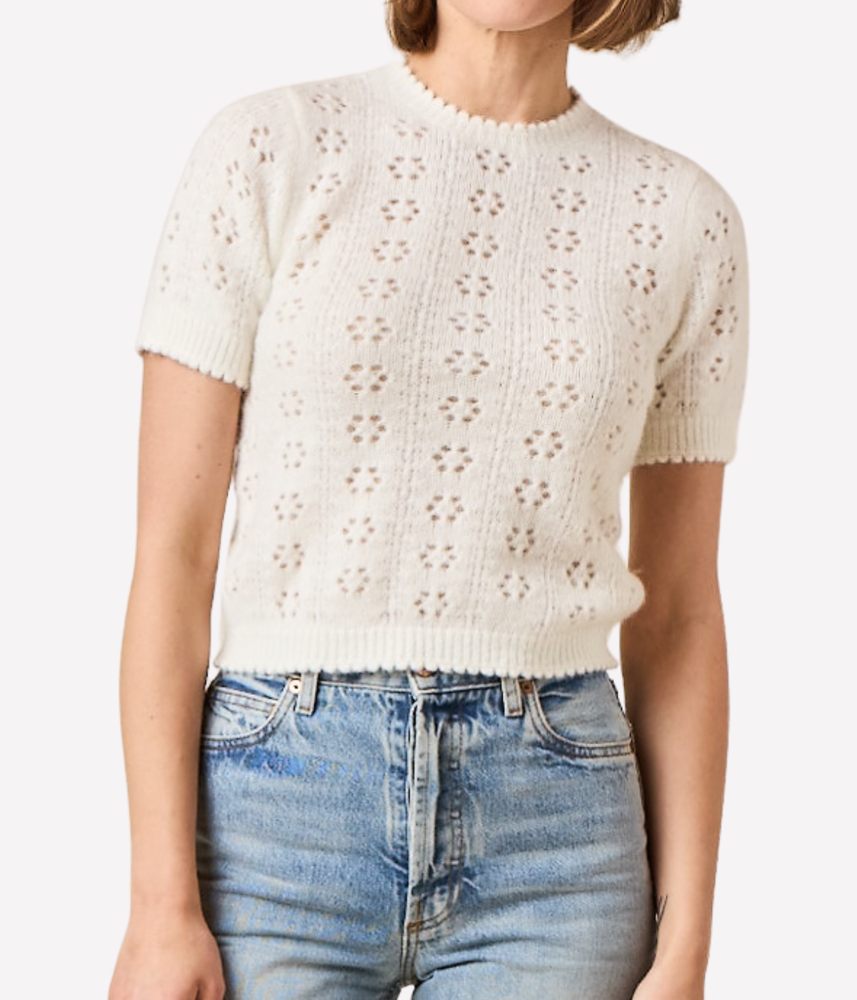 Person wearing a white short-sleeve knitted top and blue jeans on a white background