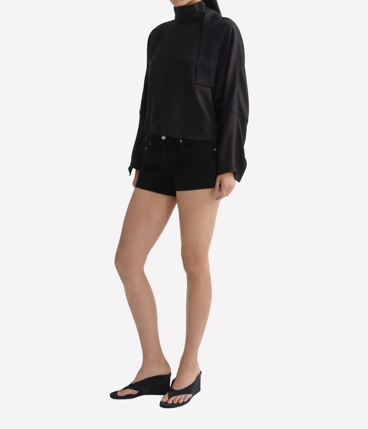 A model wearing a black long-sleeve mock-neck top with draped fabric details, paired with black denim shorts - Agolde Low Rise Parker Short in Phase